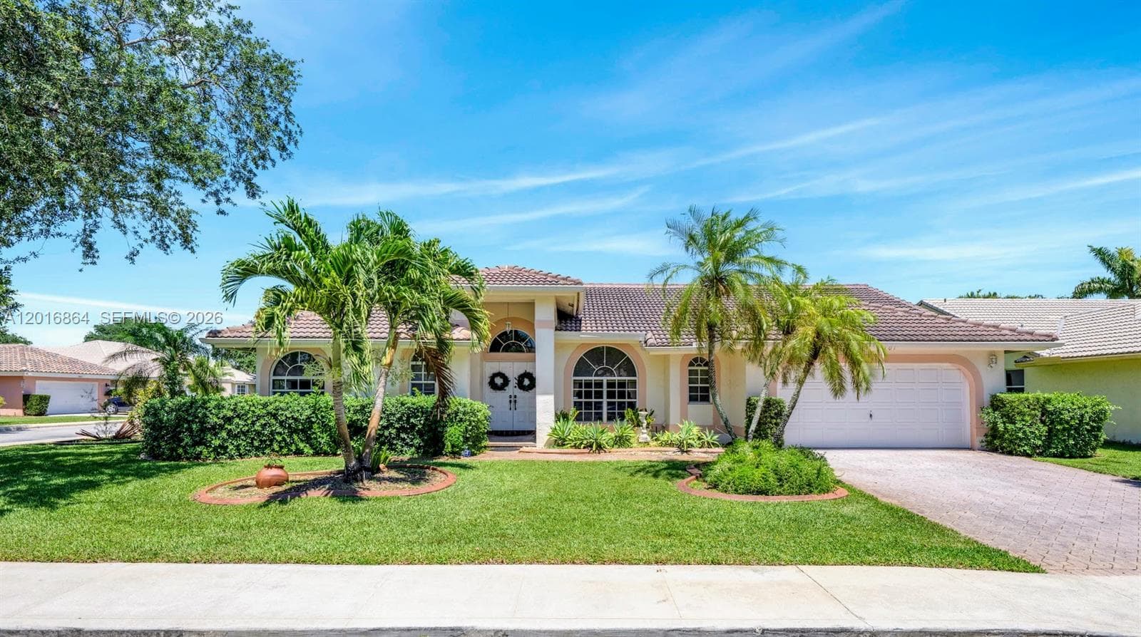 Single-story residence featuring a tile roof, arched windows, covered entryway with double doors, and a paved driveway