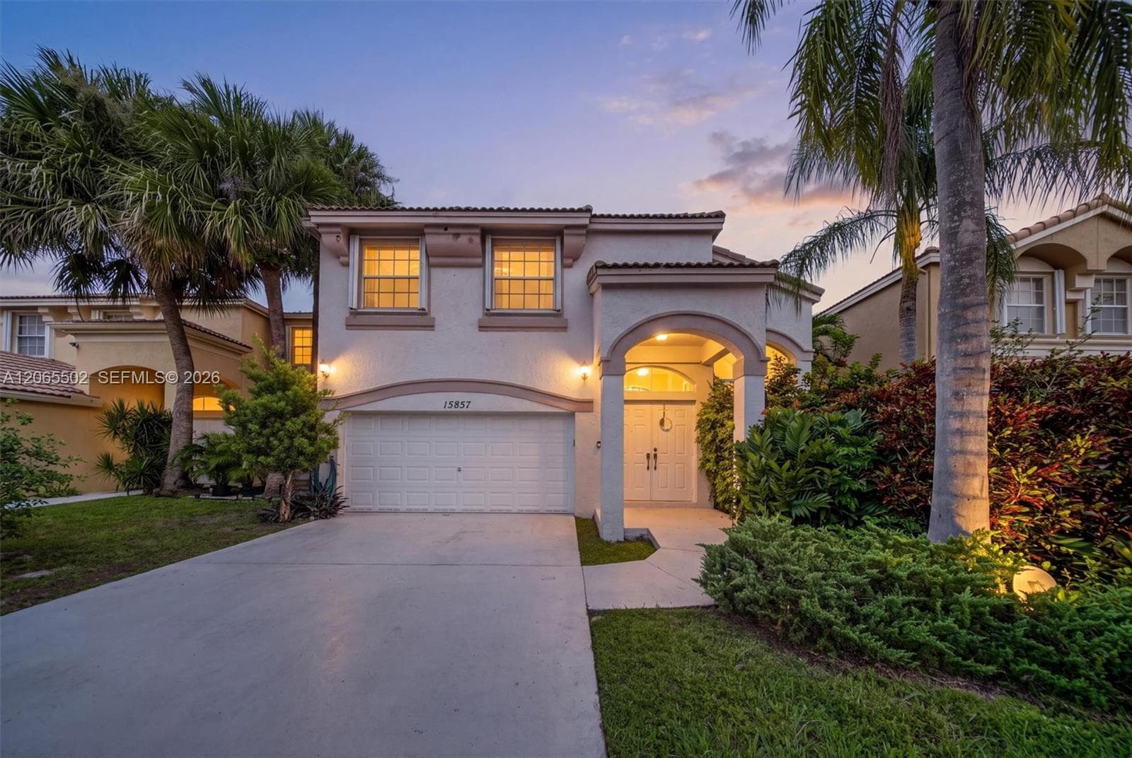 Two-story stucco exterior featuring a tiled roof, arched entryway with double front doors, and a multi-car garage