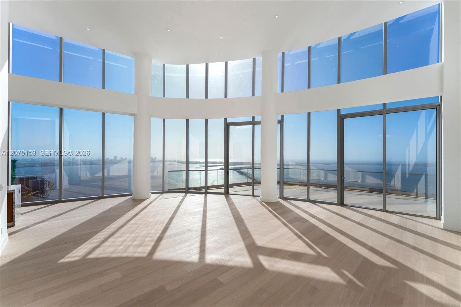 Curved wall of floor-to-ceiling windows, wood-finish flooring, recessed ceiling lighting, and structural support columns