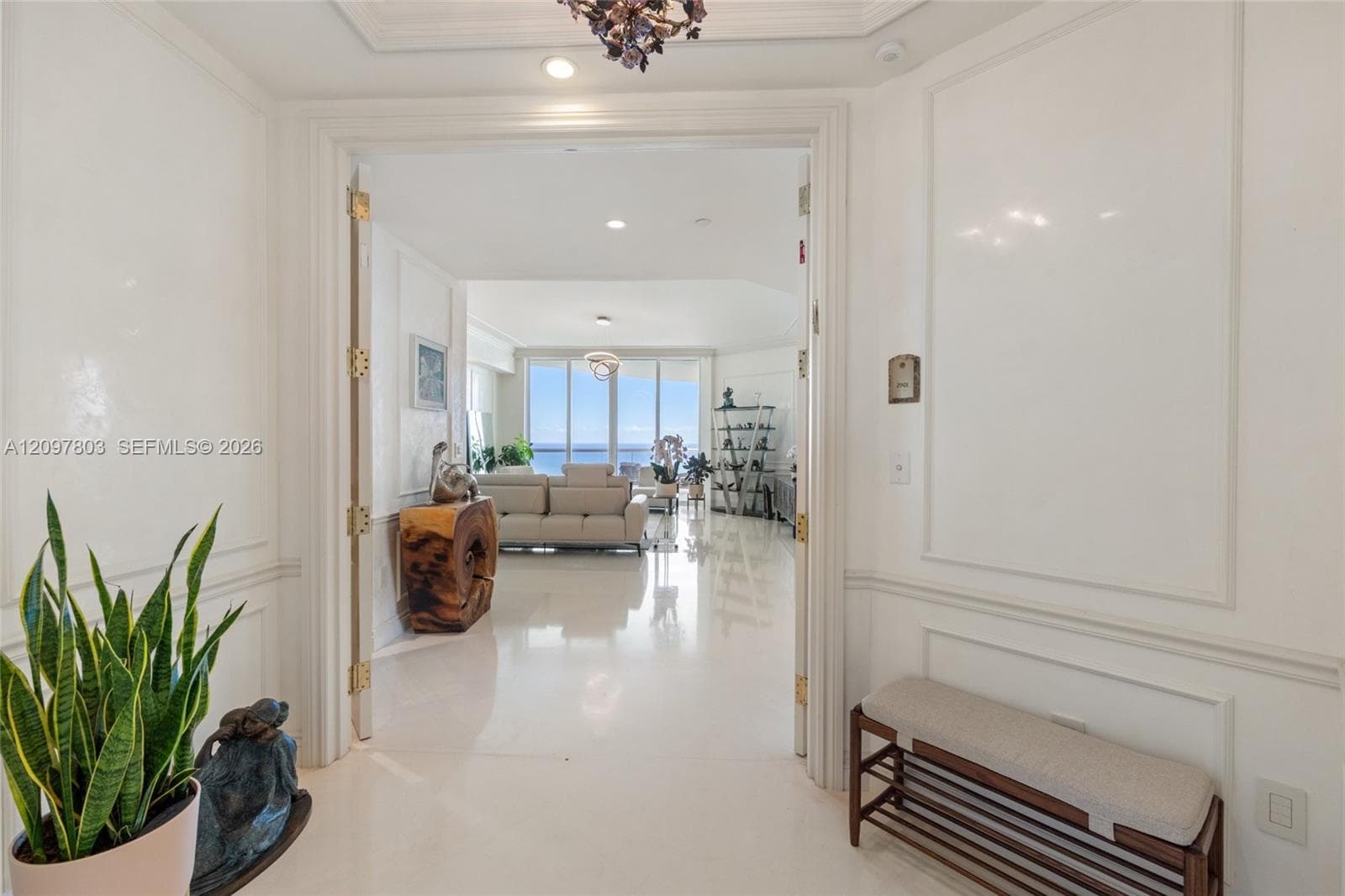 Entryway featuring polished stone flooring, custom wall molding, double doors with brass-tone hardware, and a tiered ceiling light fixture