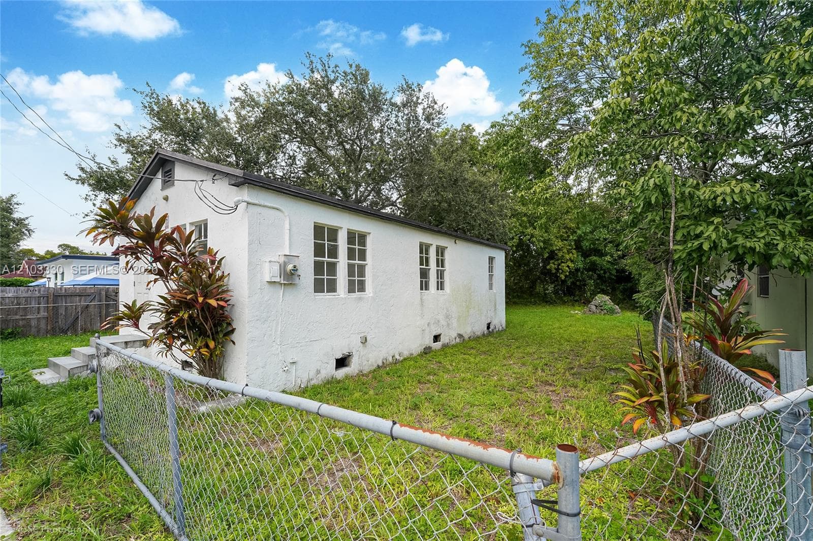 Exterior featuring white stucco siding, multi-pane windows, a peaked roofline, and chain-link fencing enclosing the grounds