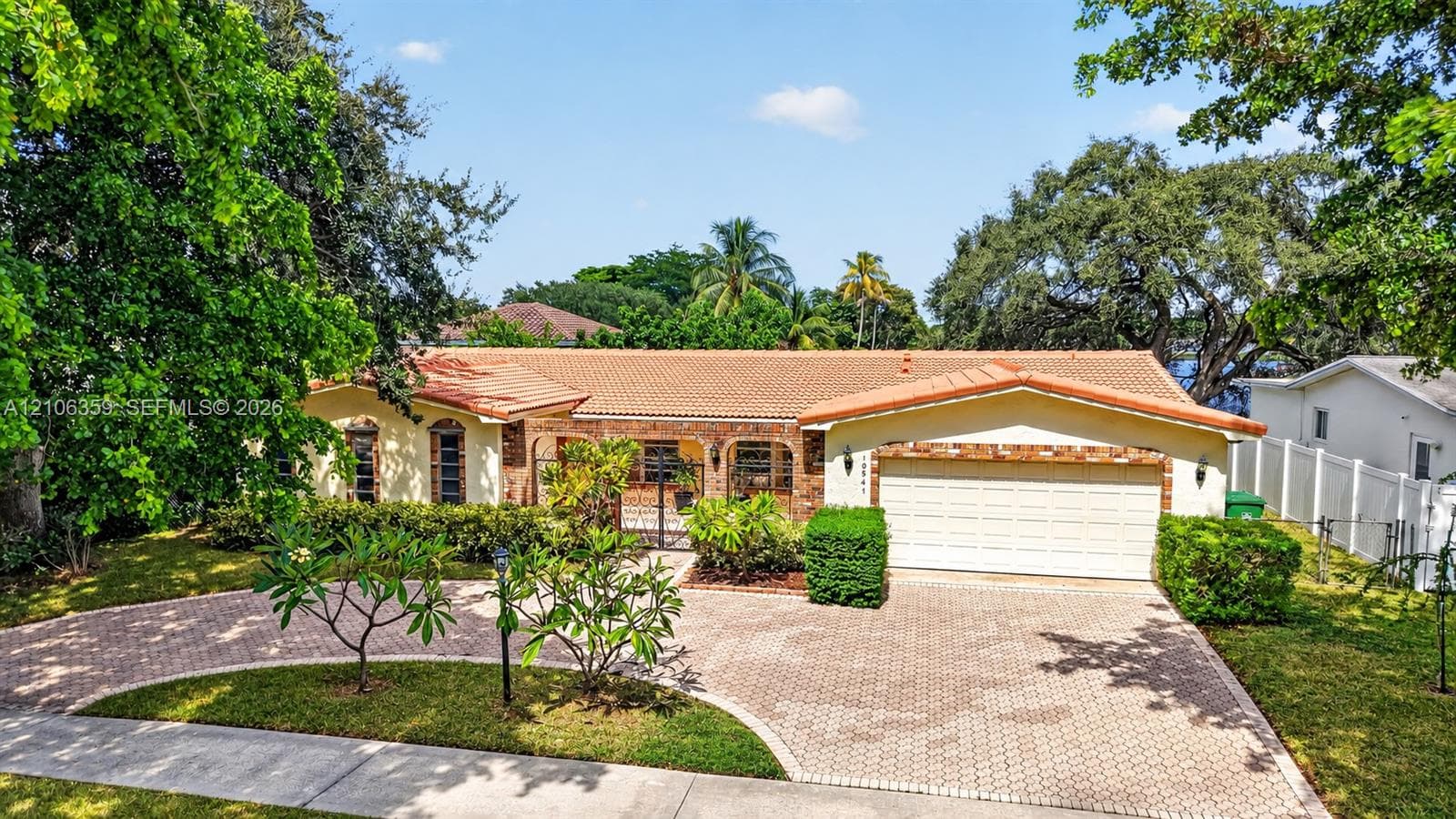 Single-story residence featuring a terracotta-tiled roof, brick exterior accents, arched entryway, and a paved stone driveway
