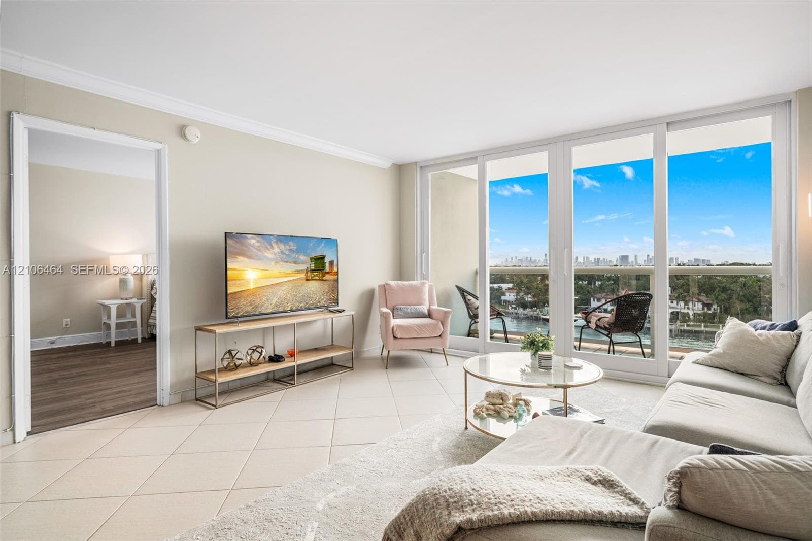 Living area featuring large-format ceramic tile flooring, crown molding, and floor-to-ceiling sliding glass doors opening to a balcony with water and city skyline scenery