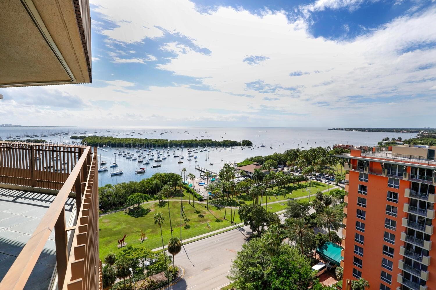 Elevated outdoor balcony with metal railing, overlooking a coastal expanse, harbor, and landscaped green space
