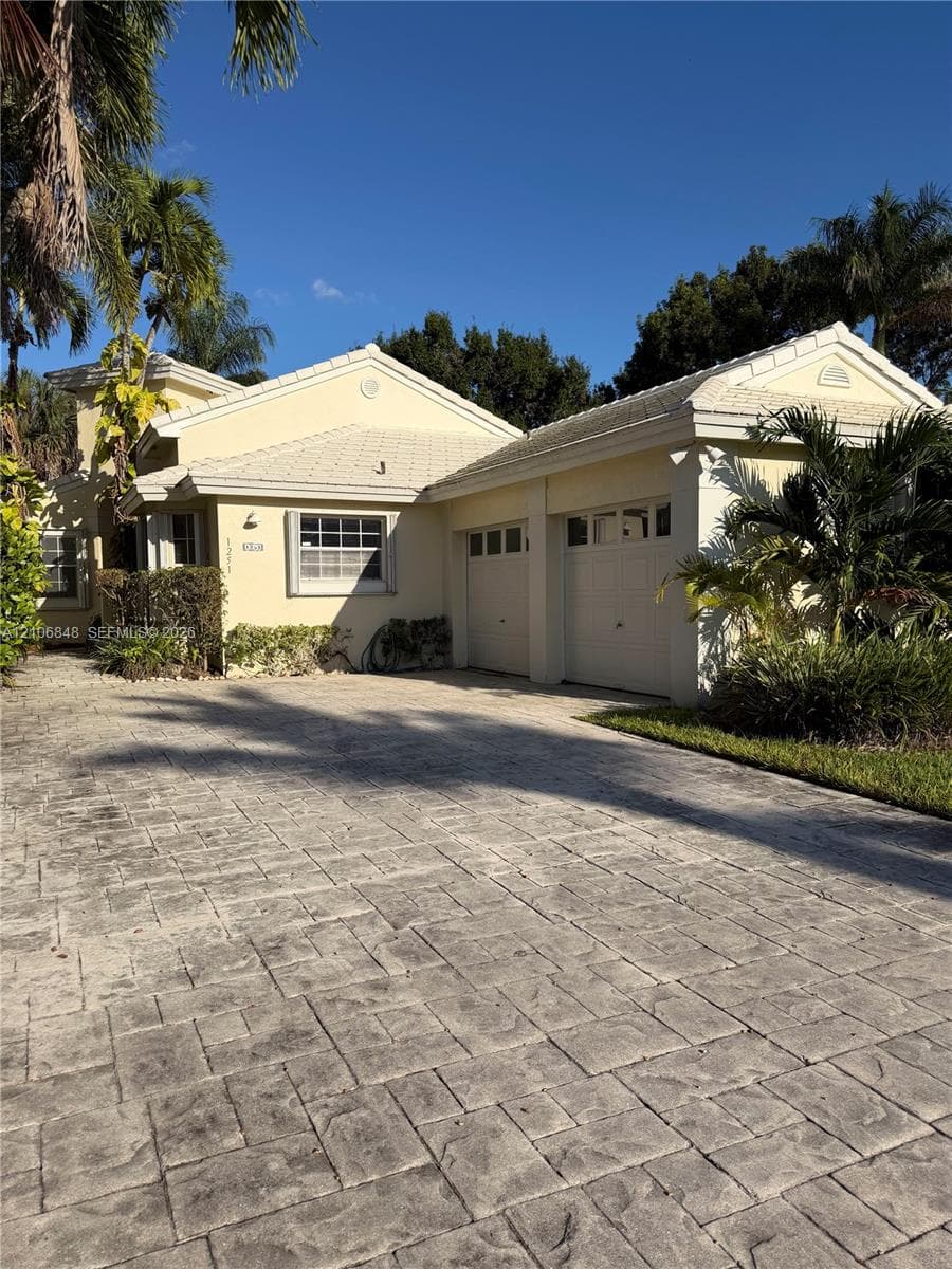 Stucco exterior residence featuring a multi-gable roofline, two-car garage, and a patterned stone-look paver driveway