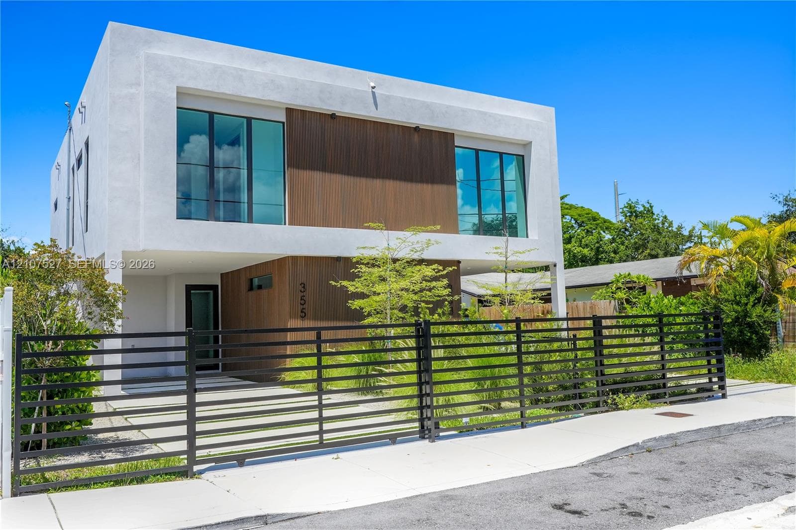 Contemporary two-story exterior featuring smooth stucco siding, wood-finish paneling, large-format glass windows, and a metal horizontal-slat security gate