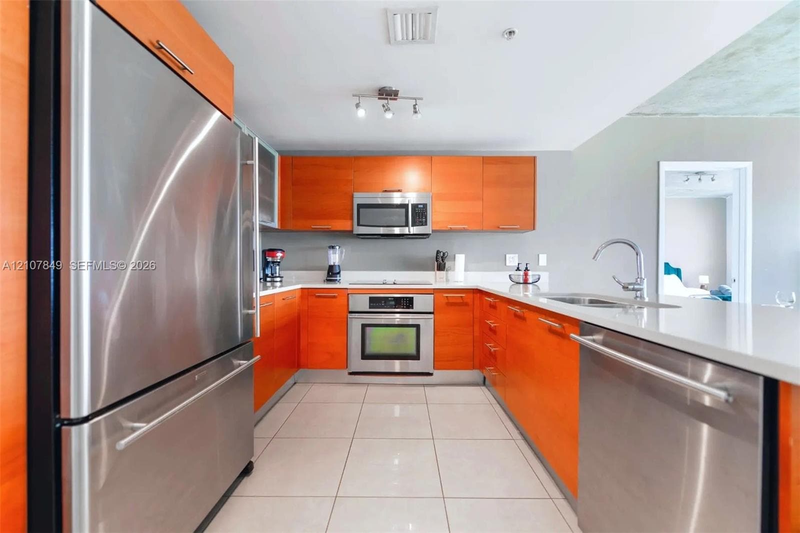 Kitchen featuring stainless steel appliances, flat-panel cabinetry, light-toned solid surface countertops, and tiled flooring