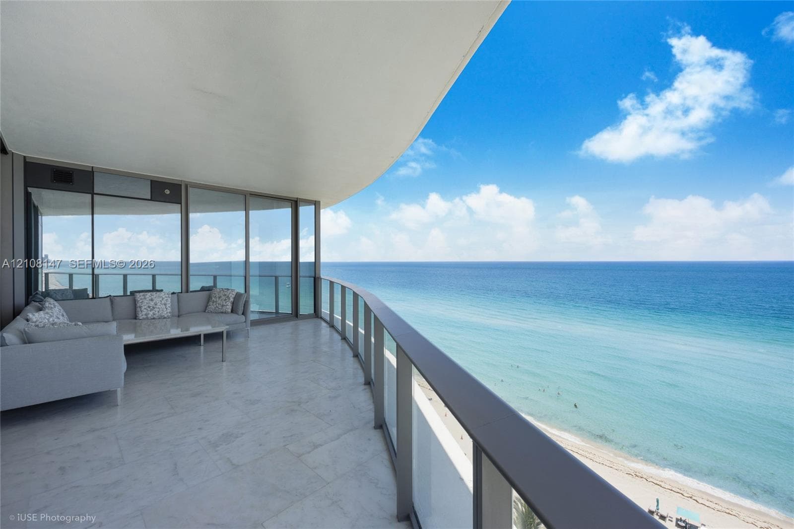 Expansive covered balcony featuring stone flooring, a glass panel railing, and full-height sliding glass doors