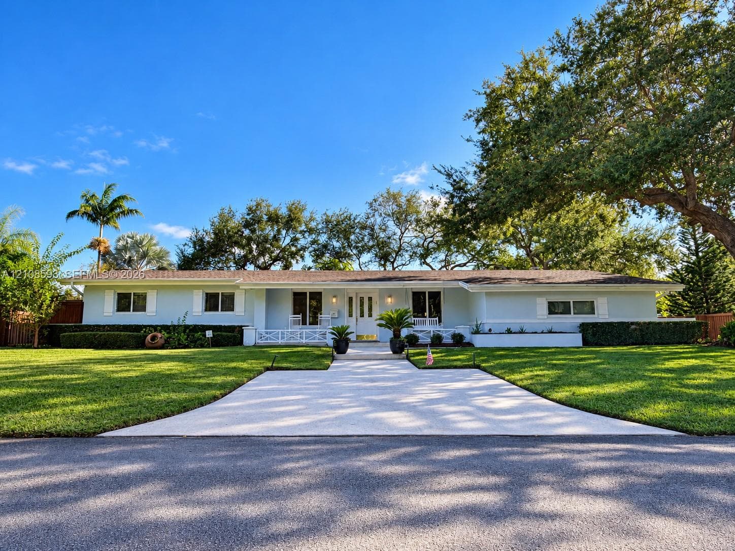 Single-story residence featuring light-toned exterior cladding, a paved walkway, covered front porch with decorative railing, and manicured landscaping