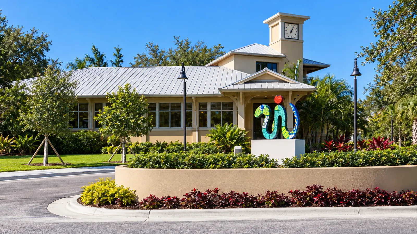 Vista ilustrativa da biblioteca de Palmetto Bay com torre do relógio e escultura colorida no Ludovici Park